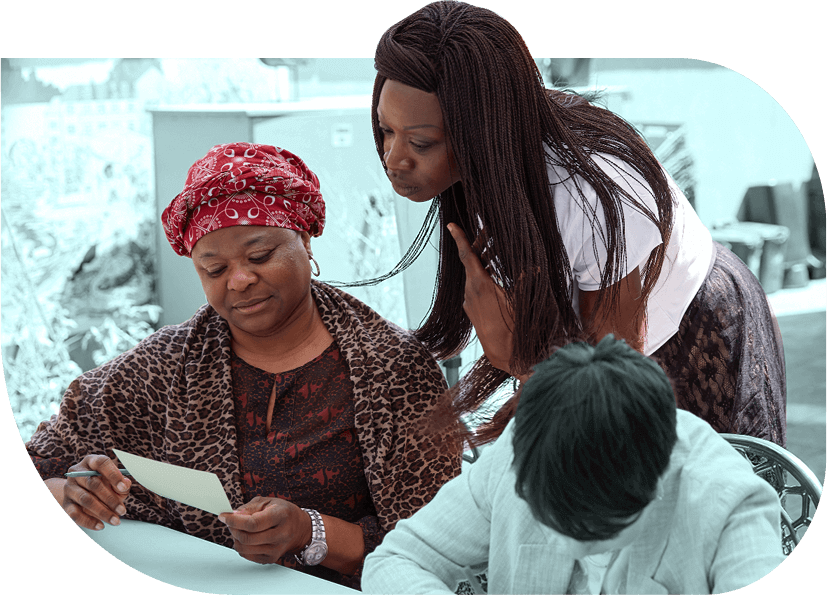 Fatou Gassama, a Black female social entrepreneur leans in to look at a piece of paper held by a Black person at an outdoor workshop.