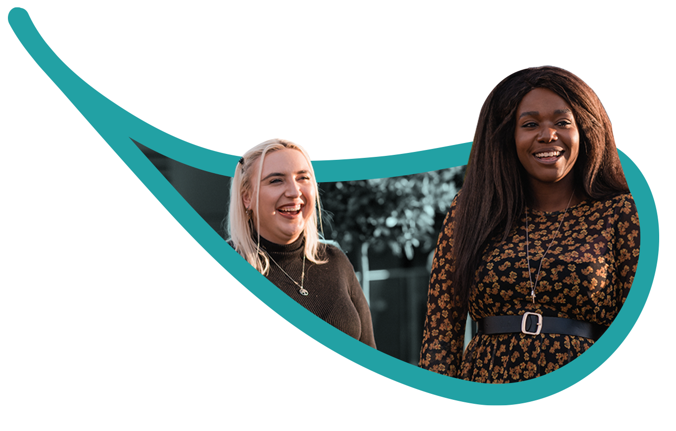 A laptop displaying the pink website homepage of Women With Wings Community Interest Company, which features a group photo of Black and Asian women smiling, holding certificates.